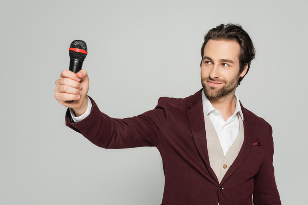 cheerful host of event in formal wear looking at microphone isolated on grey  - Foto, Bild