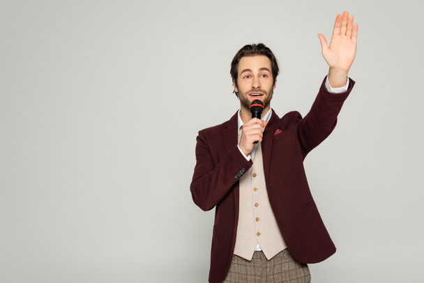 showman en ropa formal hablando en micrófono y mostrando gesto de stop aislado en gris  - Foto, Imagen