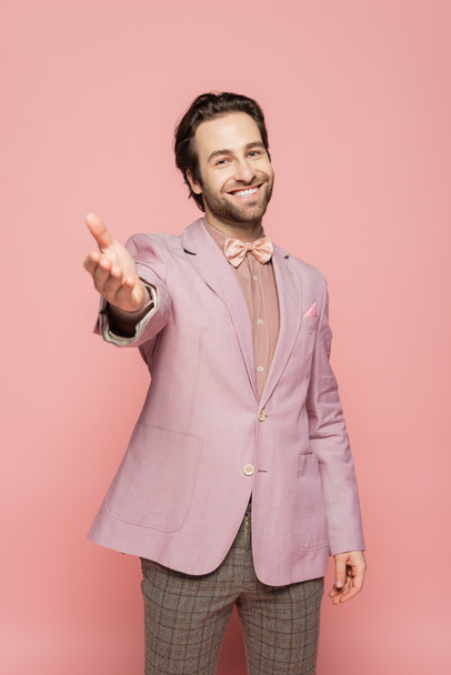 веселий і молодий шоумен у костюмі з краваткою, що стоїть з витягнутою рукою ізольовано на рожевому
  - Фото, зображення