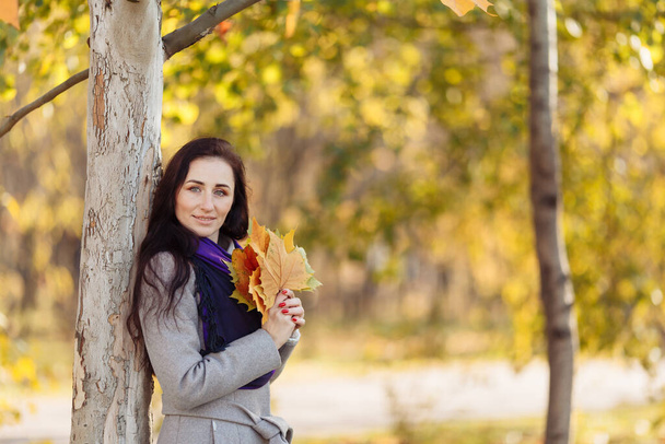 a beautiful girl with dark hair, a wet coat and a purple scarf holds a letter. blurred background and blurred leaves visible above - Photo, Image