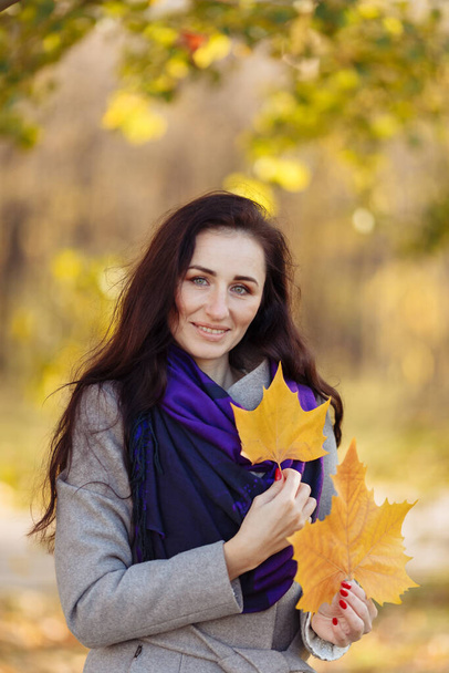 een mooi meisje met donker haar, een natte jas en een paarse sjaal houdt een brief vast. wazige achtergrond en wazig blad zichtbaar boven - Foto, afbeelding