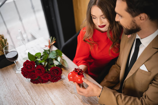 high angle view of bearded man giving heart-shaped present with bow to happy girlfriend on valentines day  - Фото, зображення