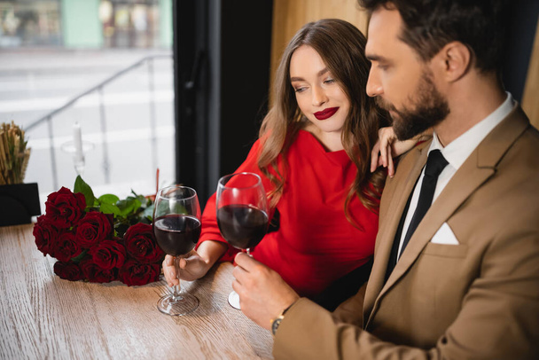 bearded man clinking glasses of red wine with happy girlfriend on valentines day  - Foto, Imagem