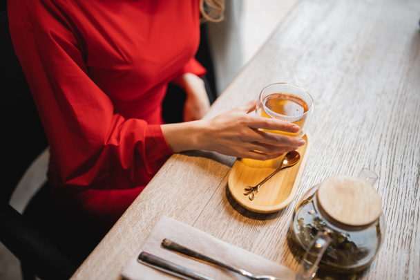 обрізаний вид жінки в червоній сукні, що тримає скляну чашку з зеленим чаєм
  - Фото, зображення