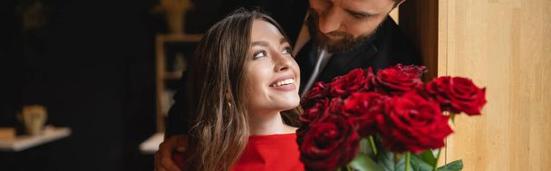 bearded man holding bouquet of red roses near happy girlfriend on valentines day, banner  - Foto, Imagem