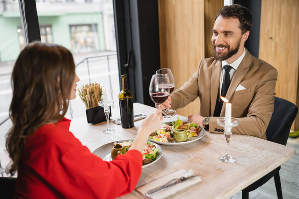 cheerful man and woman clinking glasses of red wine during dinner on valentines day - Photo, Image