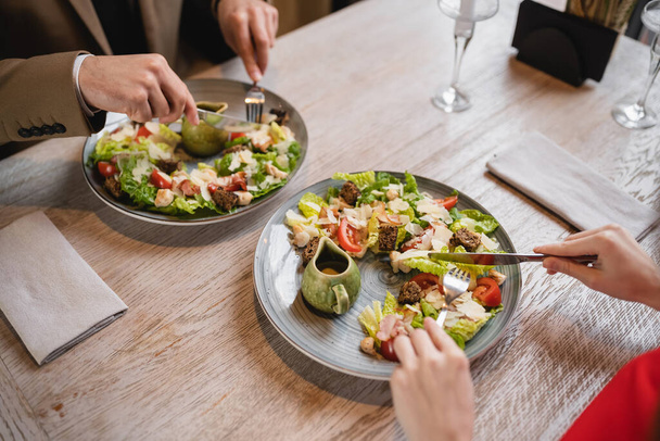 vue recadrée du couple tenant des couverts près de la salade pendant le déjeuner au restaurant  - Photo, image