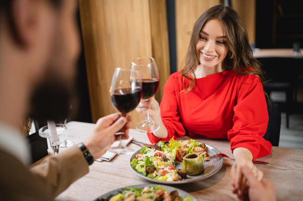 vrolijke vrouw het vasthouden van handen met vriendje terwijl klinkende bril van rode wijn  - Foto, afbeelding