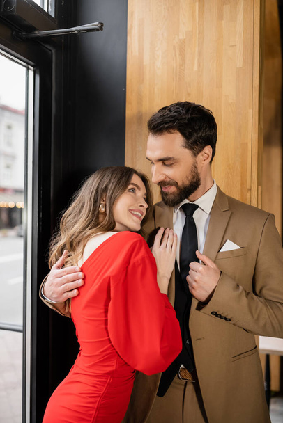 joyful and bearded man hugging cheerful girlfriend in red dress on valentines day - Photo, Image