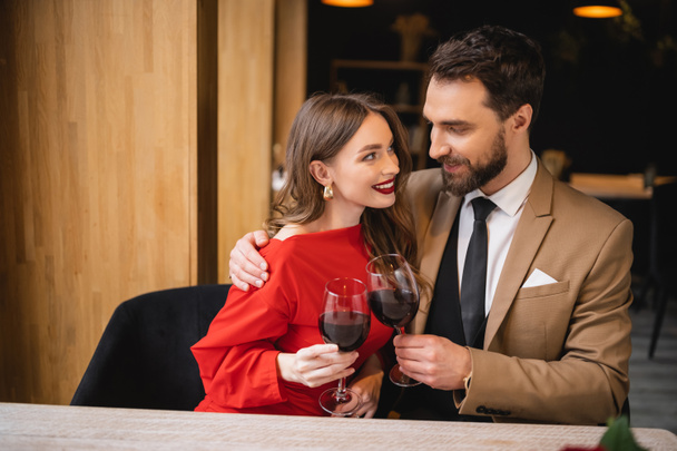 positive woman clinking glasses of wine with bearded man on valentines day - Φωτογραφία, εικόνα