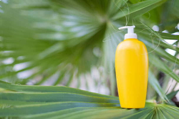 Žlutá kosmetická láhev na palmovém listu. Koncept kosmetiky nebo letních prázdnin. Mockup.  - Fotografie, Obrázek