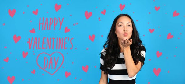 Красивая азиатка, дующая поцелуем на голубом фоне. Празднование Дня Святого Валентина - Фото, изображение