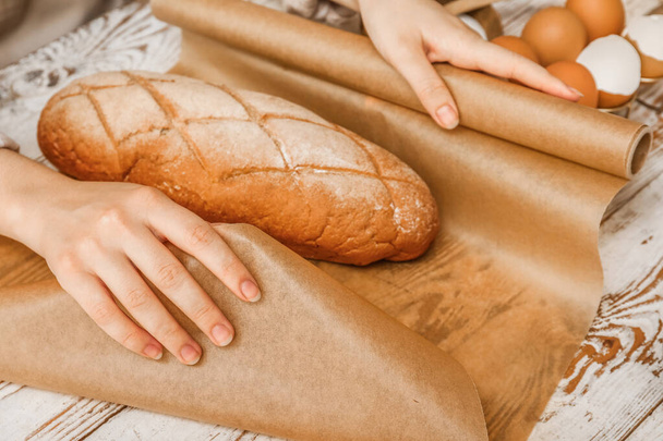 Γυναίκα περιτύλιγμα φρέσκο ψωμί με χαρτί ψησίματος σε λευκό ξύλινο φόντο, closeup - Φωτογραφία, εικόνα