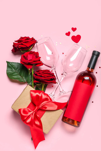 Пляшка вина, скла, троянд і подарунок на рожевому фоні. День святого Валентина. - Фото, зображення
