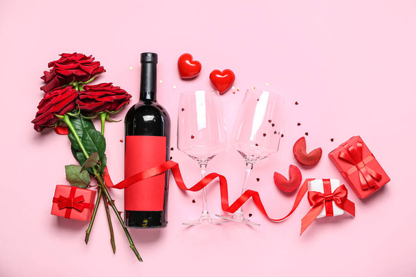 Μπουκάλι κρασί, ποτήρια, τριαντάφυλλα, κουλουράκια τύχης και δώρα σε ροζ φόντο. Γιορτή του Αγίου Βαλεντίνου - Φωτογραφία, εικόνα