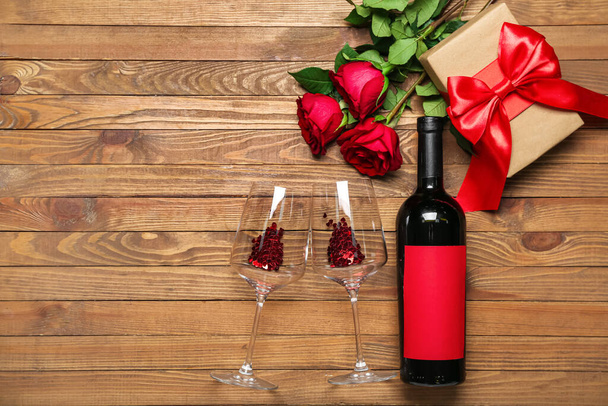 Bottle of wine, roses, gift and glasses on wooden background. Valentine's Day celebration - Photo, Image