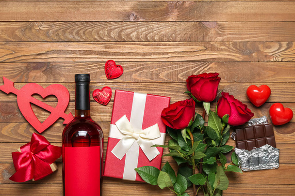 Láhev vína, růží, dárků a čokolády na dřevěném pozadí. Valentýnská oslava - Fotografie, Obrázek