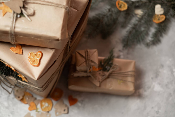 Συσκευασία των δώρων της Πρωτοχρονιάς, τα κλαδιά ελάτης και το χαρτί συσκευασίας χειροτεχνίας βρίσκονται στο τραπέζι και τυλιγμένα δώρα της Πρωτοχρονιάς σε γκρι φόντο, χαρτί χριστουγεννιάτικα δέντρα, προετοιμασία για τα Χριστούγεννα, συσκευασία δώρων έννοια - Φωτογραφία, εικόνα