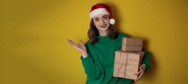 Boldog meglepett fiatal nő visel karácsonyi pulóver Mikulás kalap pózol mutató kéz karok félre jelzi a munkaterület elszigetelt egyszerű pasztell fény zöld háttér. Boldog új évet 2023 ünnep koncepció - Fotó, kép