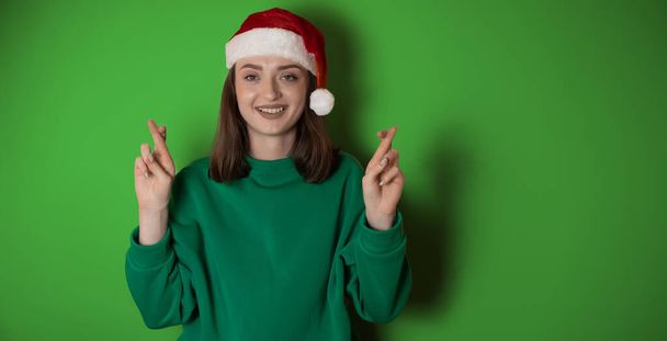 Веселая молодая женщина носить рождественский свитер Санта шляпа позировать делать жест победителя праздновать сжимать кулаки говорят да изолированы на простой пастельной светло-зеленый фон С Новым годом 2023 праздник концепции - Фото, изображение