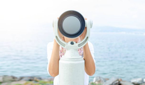 Žena se dívá dalekohledem nebo dalekohledem na pozadí moře. - Fotografie, Obrázek