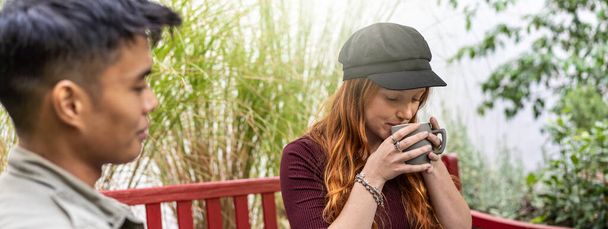 Horizontal banner or header with pensive young redhead woman drinking latte or american coffee at bar garden with multi-cultural friends - Photo, Image