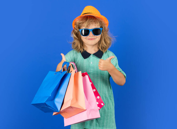 Πορτρέτο του παιδιού με τσάντα ψώνια σε μπλε απομονωμένο φόντο. Πορτρέτο ενός παιδιού με τσάντες για ψώνια. Τη Δευτέρα του Κυβερνοχώρου, μαύρη Παρασκευή. Μικρό παιδί απολαμβάνει τα ψώνια - Φωτογραφία, εικόνα