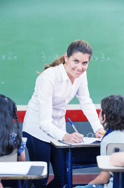 Gelukkig vrouwelijke leraar controleren studenten werk op de basisschool - Foto, afbeelding