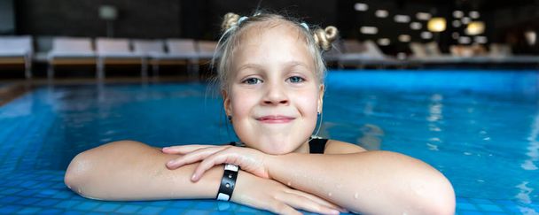 Close-up portrait little cute adorable blond caucasian happy kid girl enjoy have fun play clear blue water indoor swimming pool edge dark evening time. Child healthy lifestyle sport activity. - Foto, afbeelding