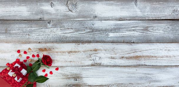 Saint-Valentin avec concept romantique composé d'une enveloppe remplie de petits cœurs d'or et de rouge se déversant sur un fond de bois rustique blanc plus cadeau et fleur de rose  - Photo, image