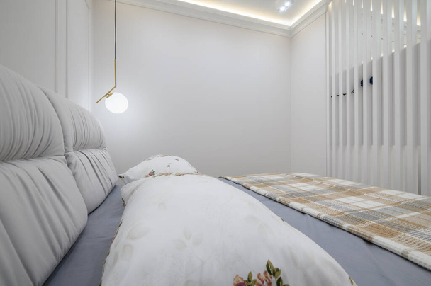 Close-up tot tweepersoonsbed met een ruitdeken en kussens erop in een gezellige slaapkamer met witte muren en een verlichtingsarmaturen - Foto, afbeelding
