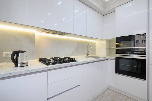 Valkoinen moderni keittiö, jossa liesi, uuni ja mikroaaltouuni, lasi vedenkeitin työtasolla - Valokuva, kuva