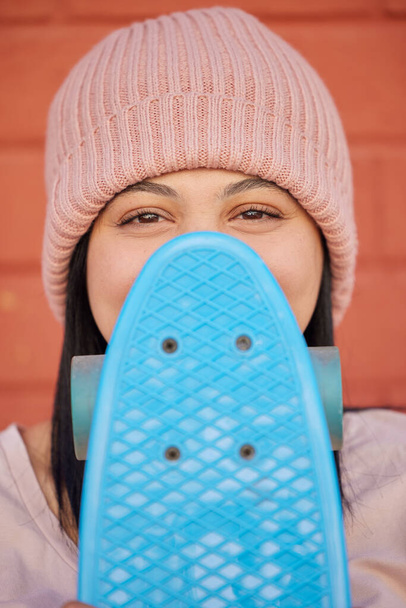 Скейтборд, молодое лицо и женщина, скрывающаяся под зимней одеждой и модой, хипстерская культура и счастье в городе. Портрет, счастливая и застенчивая девочка-фигуристка, глаза и отдых для развлечения в скейт-парке. - Фото, изображение