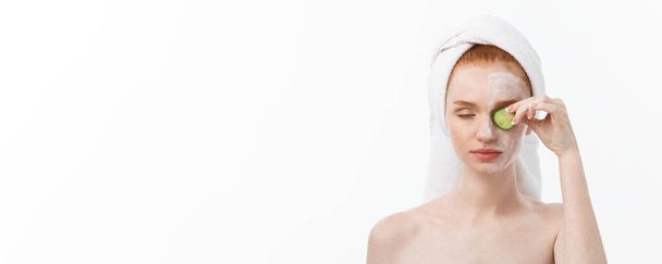 attraktive junge Frau mit schöner, sauberer Haut. weiße Maske und Gurken. Schönheitsbehandlungen und kosmetologische Wellnesstherapie. weißer Hintergrund. - Foto, Bild