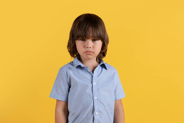 Koncept dětské psychoterapie. Studio portrét rozrušeného chlapečka trpícího šikanou a společenskými problémy, smutně hledící do kamery, oranžové pozadí, volné místo - Fotografie, Obrázek