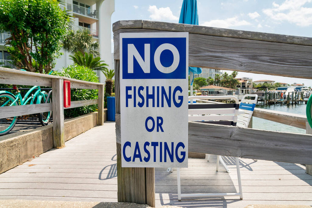 No fishing or casting sign on a wood railings at Destin, Florida. Close-up of a sign against the view of chairs and wooden deck near the water. - Photo, Image