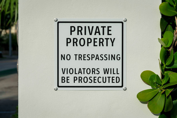 Własność prywatna Zakaz wtargnięcia Przestępcy będą ścigani na tabliczce przy ścianie Miami, FL. Zbliżenie znaku umieszczonego na białej ścianie w pobliżu roślin po prawej stronie. - Zdjęcie, obraz