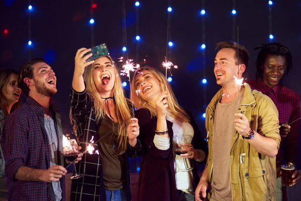 Grab a sparkler and smile for the selfie. a group of friends taking a selfie while having fun at a nightclub - Photo, Image