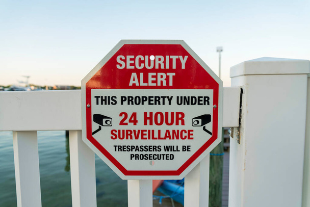 Ochrona ostrzega tę nieruchomość pod 24 godzinnym znakiem obserwacji na balustradzie w Destin na Florydzie. Zbliżenie oznakowania prywatnej nieruchomości w pobliżu morza. - Zdjęcie, obraz