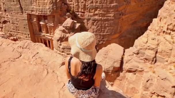 Vicino viaggiatore turistico caucasico sedersi sul punto di vista sopra Petra antica città guardando il Tesoro o Al-Khazneh, famosa destinazione di viaggio della Giordania. Patrimonio Mondiale UNESCO - Filmati, video