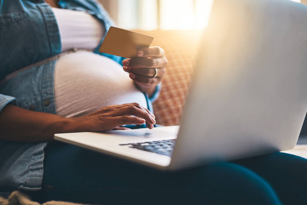 Собираюсь до того, как родится ребенок. беременная женщина с помощью ноутбука и кредитной карты на диване дома - Фото, изображение