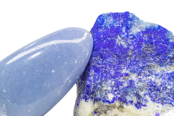 Macro light blue angelite crystal, shiny tumbled blue anhydrite stone and a deep royal blue lapis lazuli mineral with gold pyrite specks and white calcite veins isolated on a white surface background. Two blue crystals, angelite and lapis lazuli.  - Photo, image