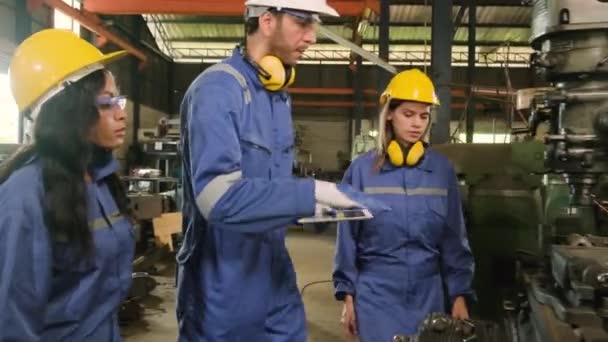 Egy ipari munkás csapat védő- és biztonsági egyenruhában és keménykalapban, férfi menedzser, és kollégái sétálnak és fémmunkáról beszélgetnek a gyárban. Profi gyártásmérnök. - Felvétel, videó