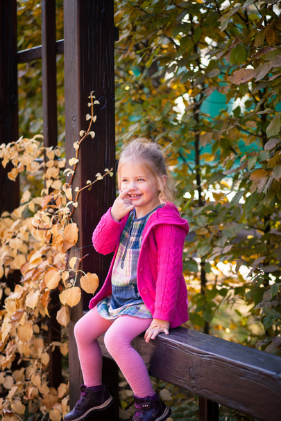 Lächelndes lustiges kleines Mädchen in heller Kleidung, das sich die Nase zupft - Foto, Bild