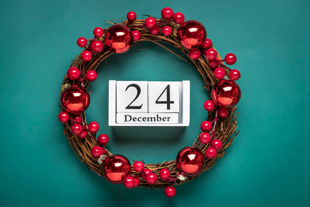 Karácsonyi koszorú díszített piros bogyók, fa naptár dátum 24 December elszigetelt zöld háttér koncepciója karácsonyi felkészülés, hangulat Kívánságkártya Kézzel készített karácsonyi koszorú Lapos fektetés. - Fotó, kép