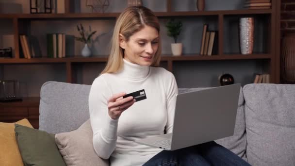 Ziemlich glückliches Mädchen macht Online-Zahlung mit Kreditkarte mit modernen Laptop zu Hause auf dem Sofa sitzend und lächelnd. Finanzen, Einkaufen im Internet-Online-Banking E-Commerce-Konzept - Filmmaterial, Video