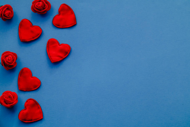 Κόκκινες καρδιές και κόκκινα τριαντάφυλλα σε μπλε φόντο. Ημέρα του Αγίου Βαλεντίνου κάρτα χαιρετισμού. Αντιγραφή χώρου. - Φωτογραφία, εικόνα