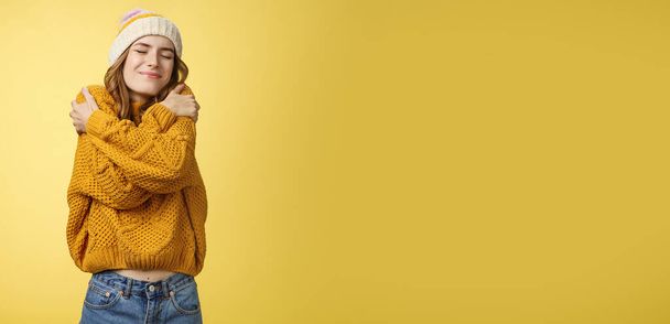 Upbeat charming cheerful young woman feeling lucky happy embracing herself like new warm comfortable sweater tilting head shoulder close eyes smiling broadly hugging own body, yellow background. - Photo, Image