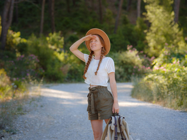 Fehér gyömbér fiatal gyönyörű női hátizsák utazó egyedül az erdőben. Vonzó utazó nézzen körül, és fedezze fel, miközben séta a természetben fa boldogsággal és szórakozással nyaralás utazás közben. - Fotó, kép