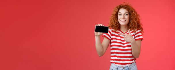 Aufgeregt glücklich gut aussehende europäische rothaarige Lockenkopf erstaunt zeigt persönliche Leistung Ergebnis Smartphone-Spiel zeigen Handy-Bildschirm zeigt Anzeige diskutieren awesome Gameplay lächelnd erfreut. - Foto, Bild